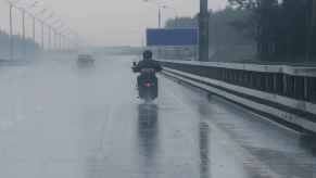 A biker riding a motorcycle away from camera on freeway in the rain