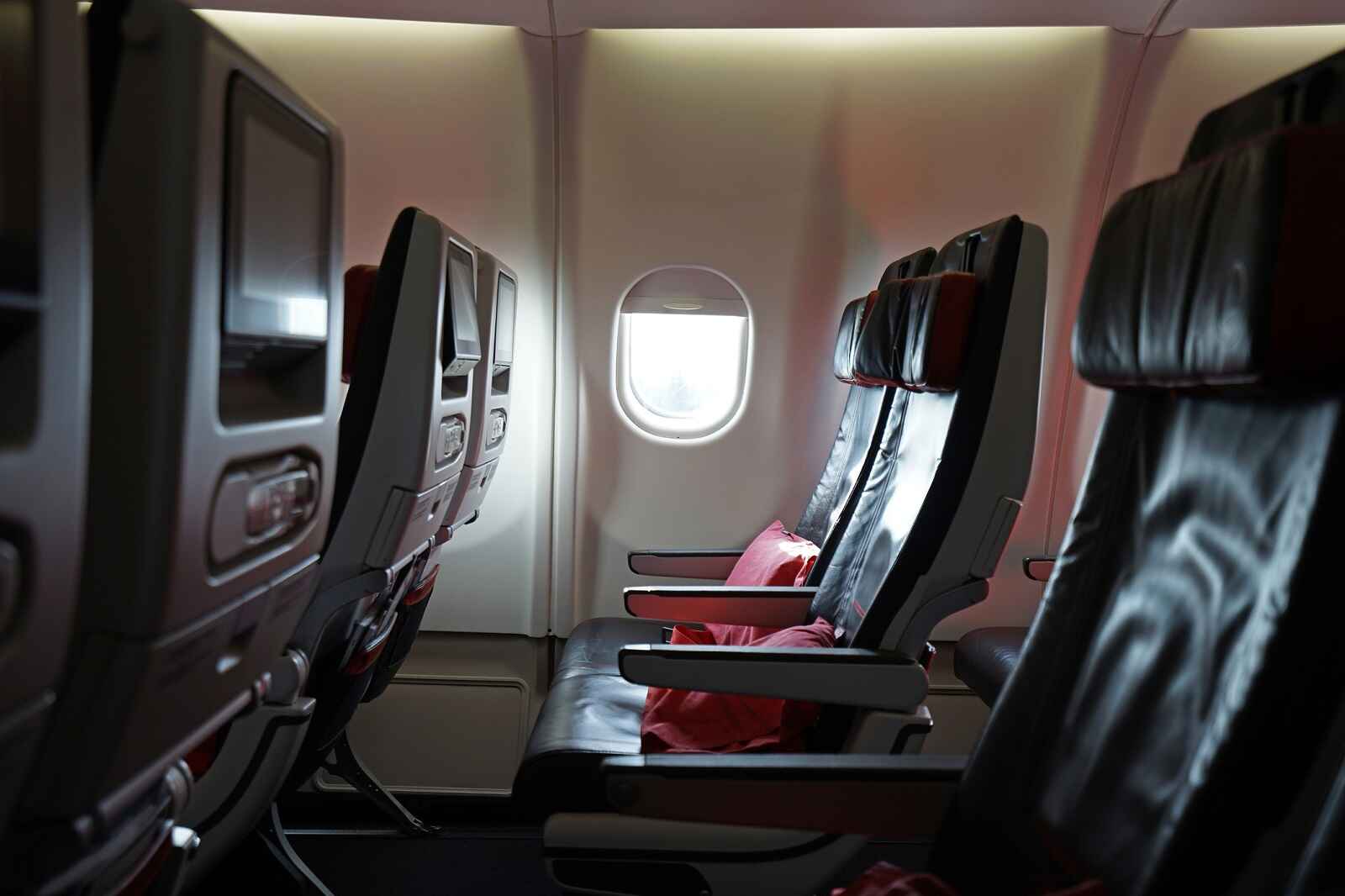 Leather airplane seats facing left profile with bright white light shining into round airplane window