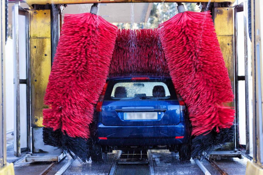 An automatic car wash cleans a blue car in rearview with big red brushes