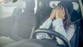 A woman sitting in the driver's seat of a car covering her face with her hands
