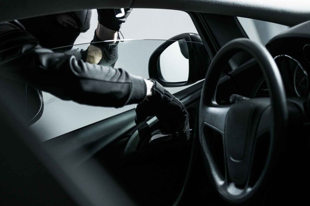 Car theft in progress a man dressed in all black opening a left front car door from the inside handle