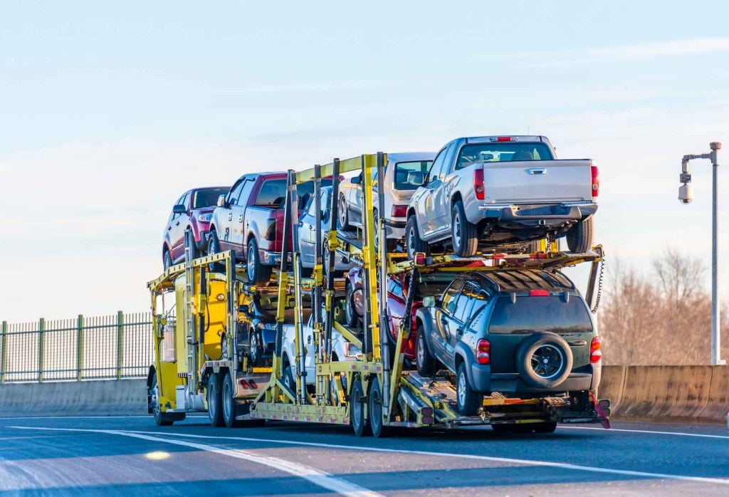 A yellow car transport truck loaded with nine vehicles, including pickup trucks, SUVs, and small cars.