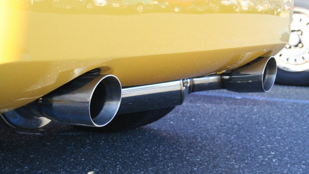 A yellow car's rear bumper shows dual exhaust tips close to the road
