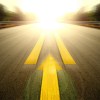 A bright sun at the end of a blurred road with high contrast orange stripes and painted arrow pointed down the road