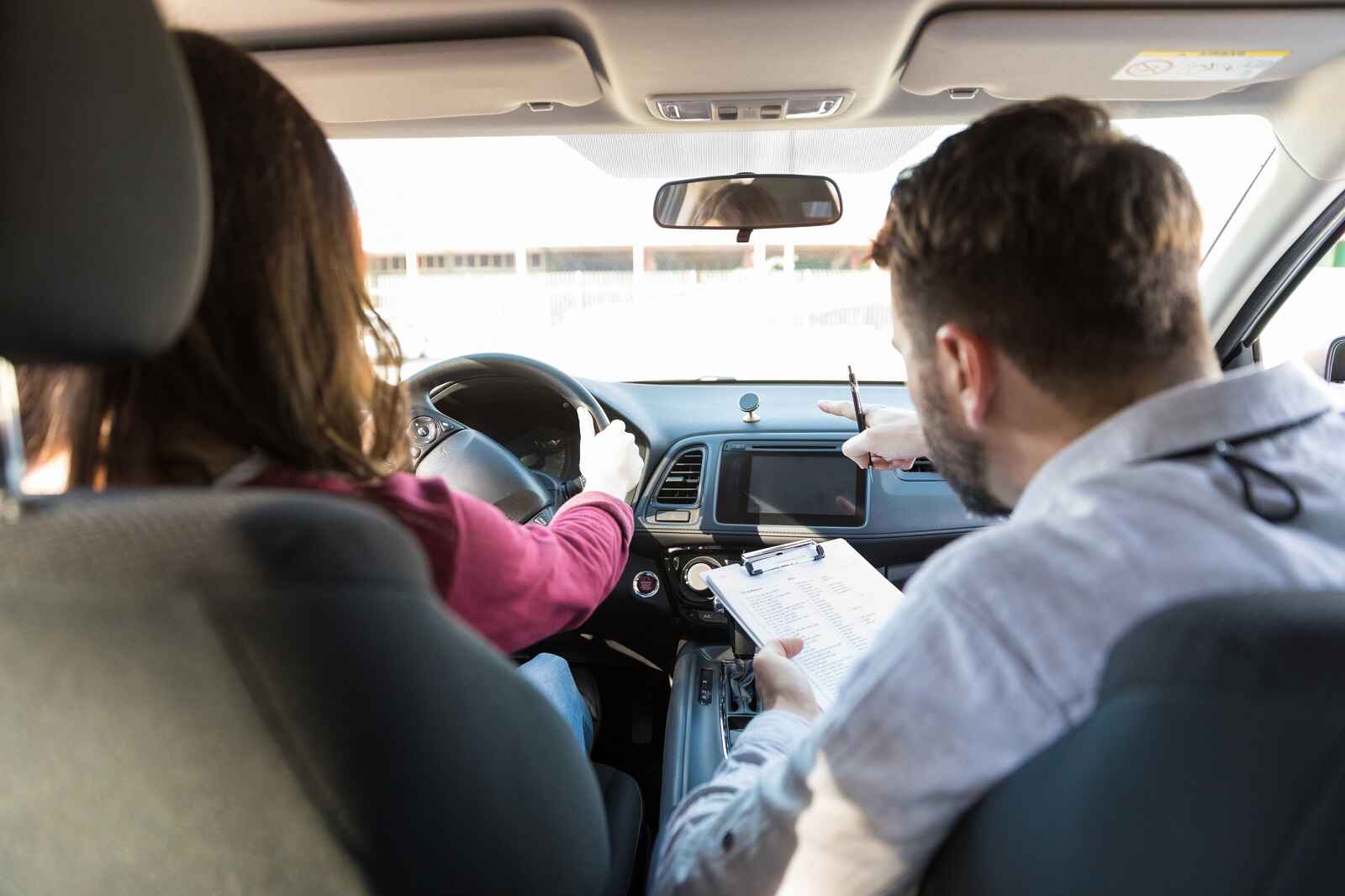 A woman takes driver's license education in a car sitting next to instructor holding a clipboard and pen