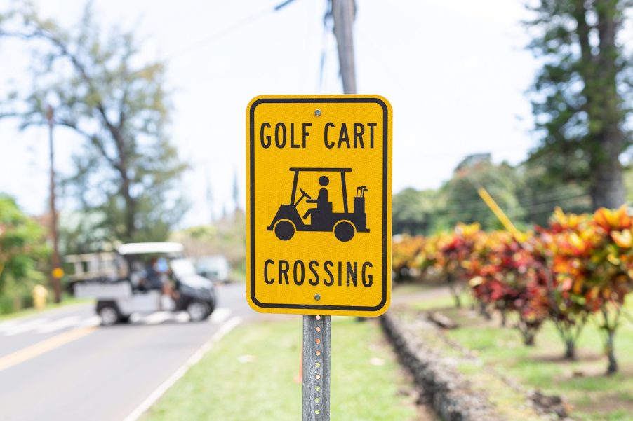 Bright yellow "Golf Cart Crossing" sign with a golf cart visible in the background.