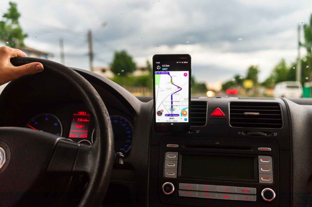 A cell phone with Google Maps "Waze" app open mounted to a car dash while driving