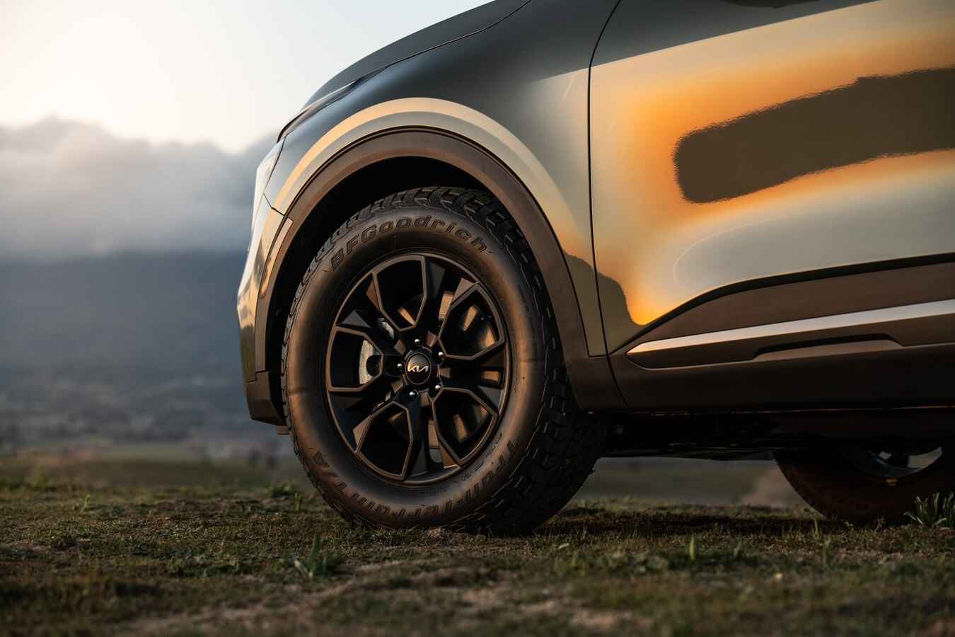 A dark colored Kia Sorento SUV photographed outside in very close view of the left front wheel, fender, and door