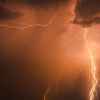 Orange lightning bolts striking a black-colored sky and clouds