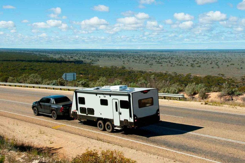 A dark pickup truck towing a boxy camper in a desert environment on the highway