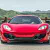 A red 2012 McLaren 12C coupe sits in direct front view green mountains in the background