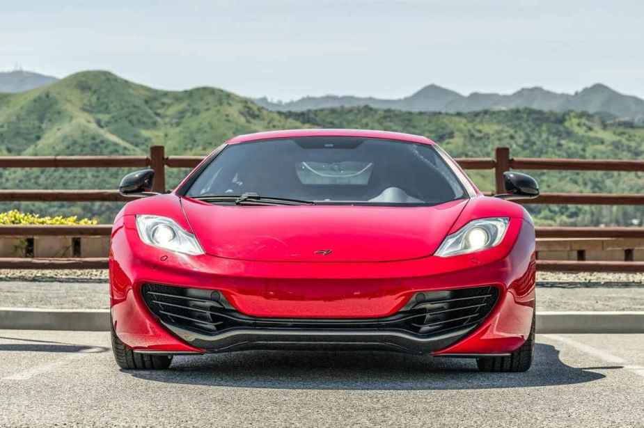 A red 2012 McLaren 12C coupe sits in direct front view green mountains in the background