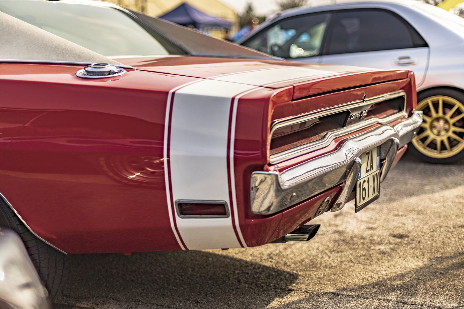A the back half of a red restomod Dodge Charger classic car with a white stripe at a car meet in Italy