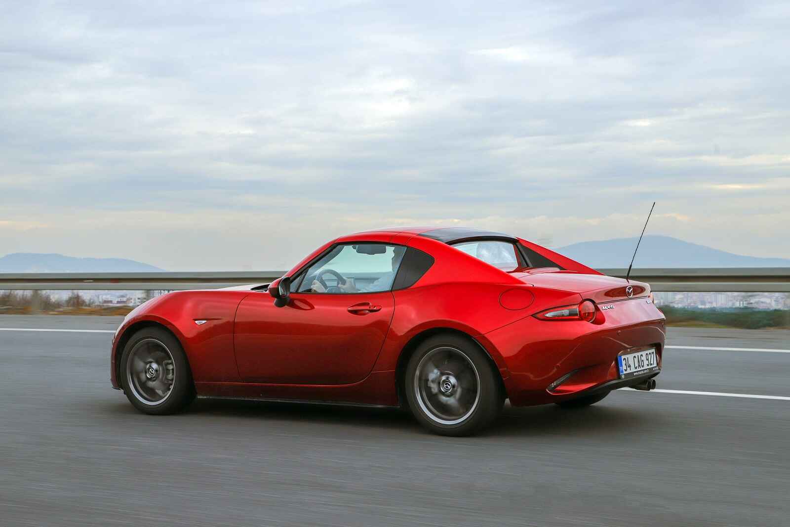 A red roadster, a Mazda Miata, driving on a freeway with mountains in the background