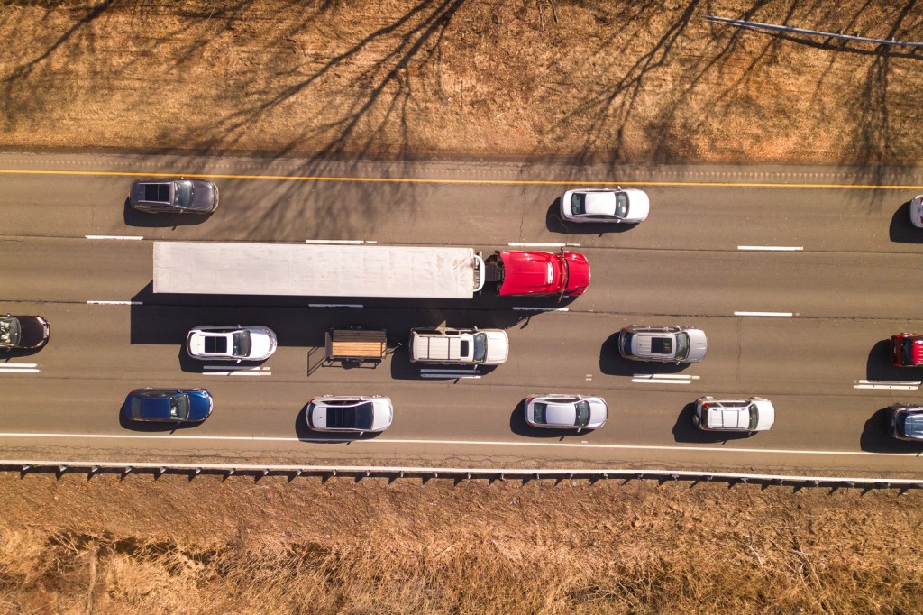 An aerial view of a red semi-truck driving on highway surrounded by other cars