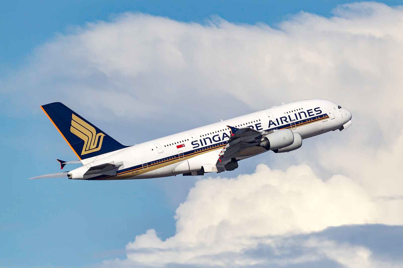 A Singapore Airlines plane flying in full right profile view in cloudy blue skies