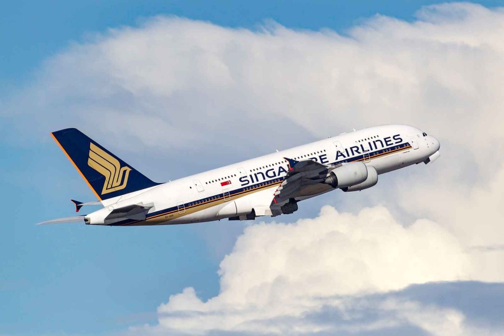 A Singapore Airlines plane flying in full right profile view in cloudy blue skies