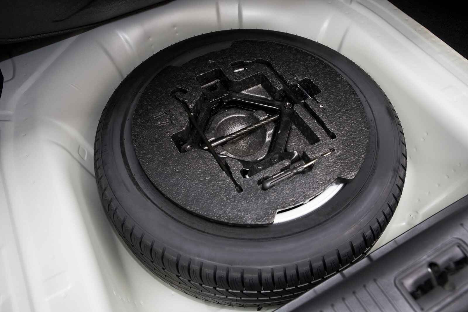 A black spare tire with tools mounted on top inside a car trunk