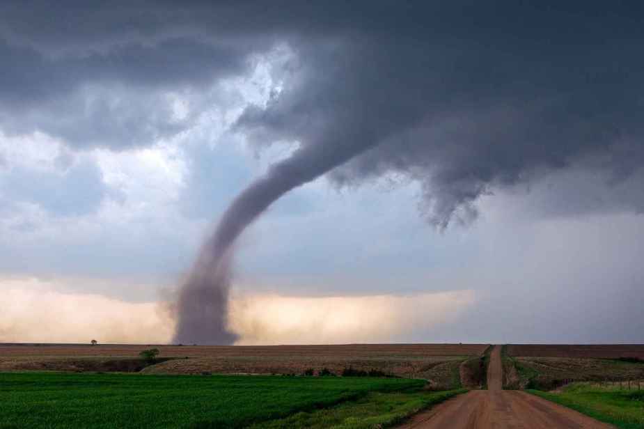 A full tornado shown touching down in a rural scene with a dirt road to the right frame