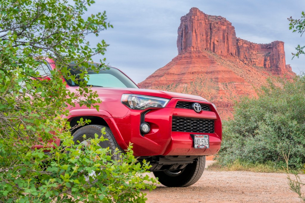 A red Toyota 4Runner nose peeking out from brush with a sandstone butte in the background