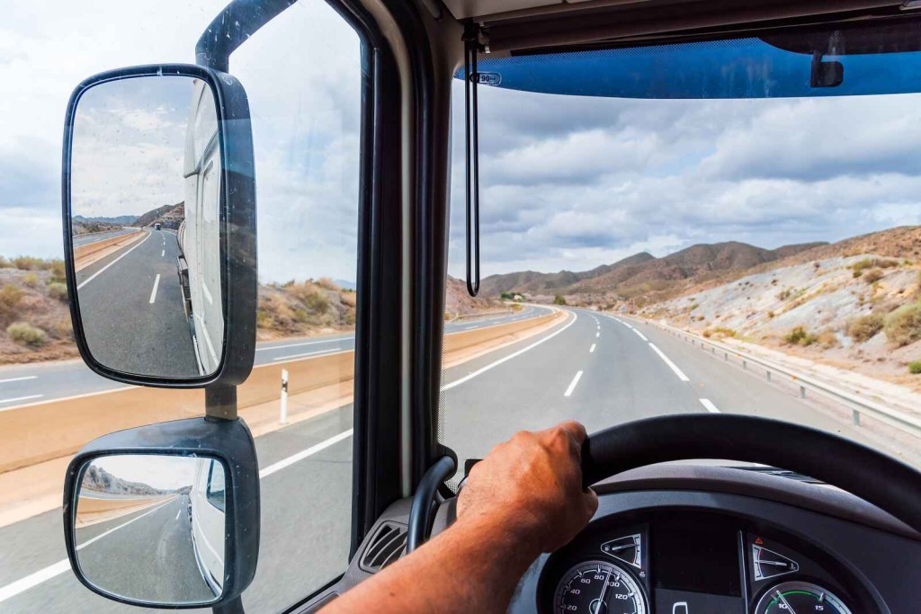 A truck driver drives on hilly desert road from driver's perspective