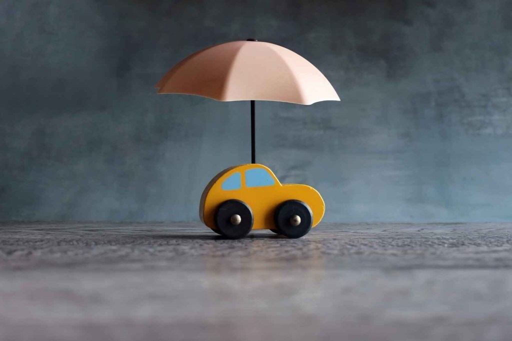 A yellow wooden toy car on a flat surface with a toy umbrella placed open on the car roof