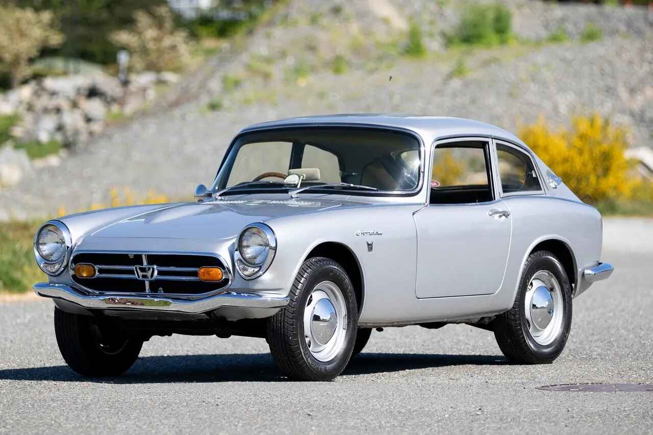 Silver 1968 Honda S800 coupe, one of several classic Honda sports cars, parked in left front angle view on road with gravely hill in background