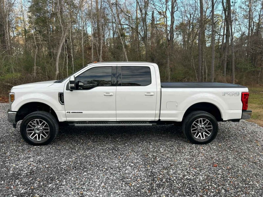 A white Ford F-250 pickup truck parked on gravel in left profile view