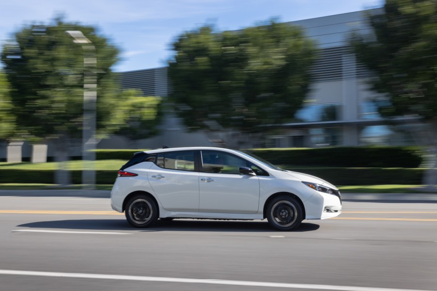 A white Nissan LEAF drives down an empty street.