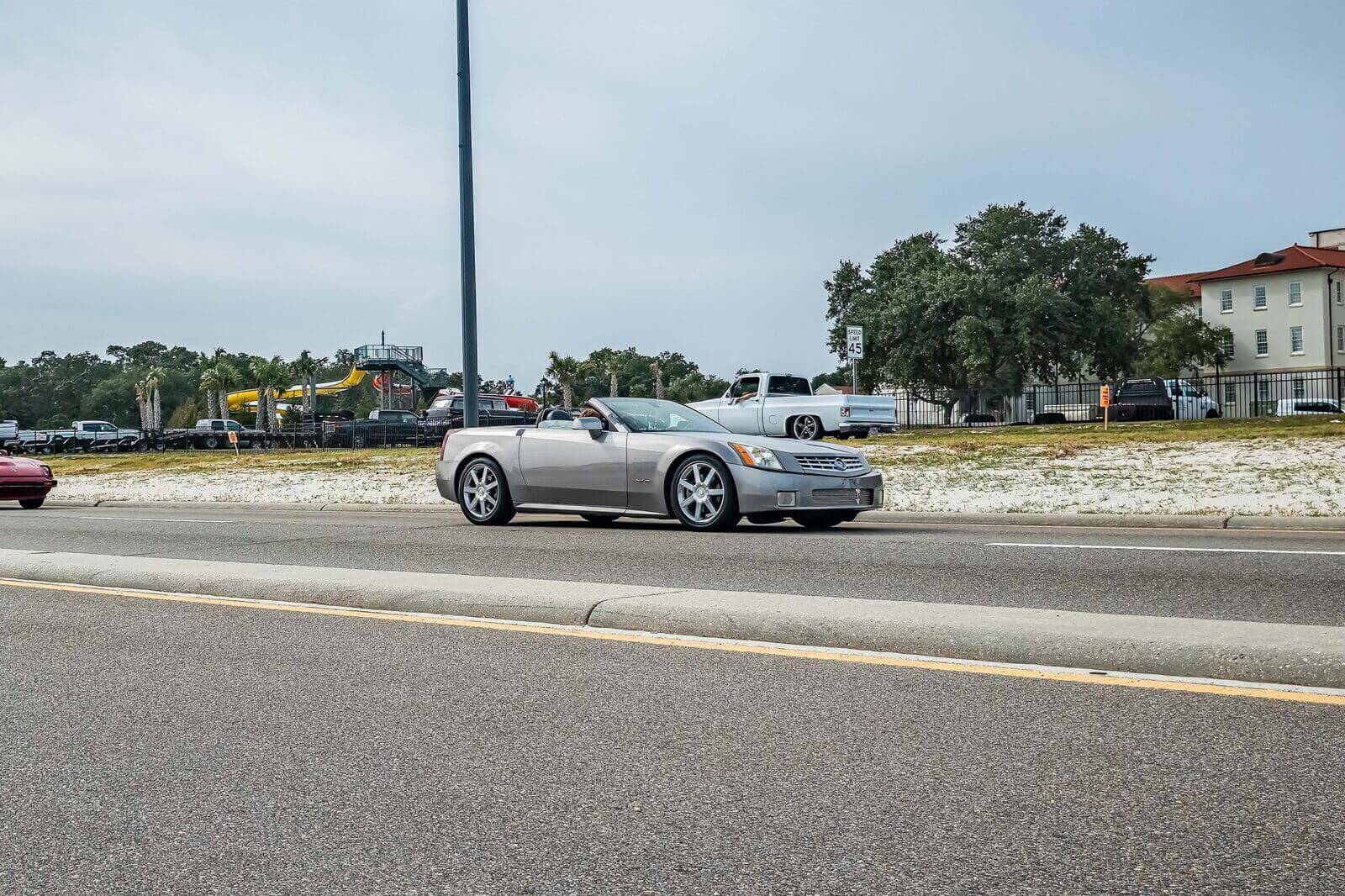 A silver Cadillac XLR convertible, a sibling to the Corvette, drives down the road. 