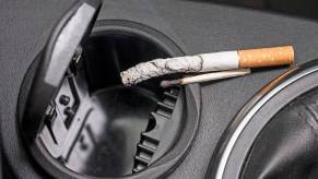 Cigarette balancing on the ashtray of a car's center console.