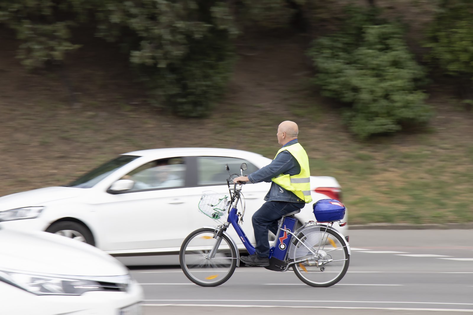 Man rides an e-bike through traffic, a white car visible in the background.