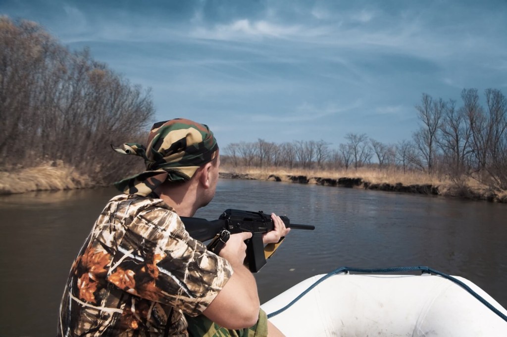 A hunter with a magazine-fed Kalashnikov-style shotgun on an inflatable vessel