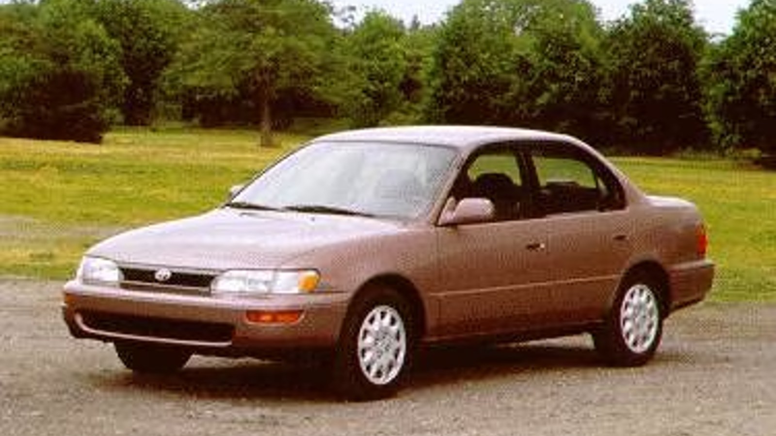 Tan 1995 Toyota Corolla posed on a gravel driveway.
