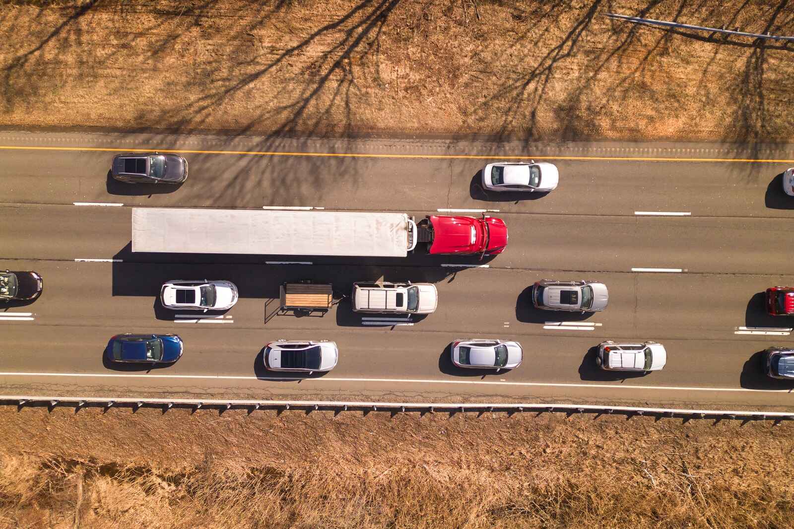 Aerial view of a semi-truck surrounded by passenger cars on a four-lane highway