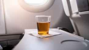 A cup of alcohol that appears to be neat whiskey on a napkin on a plane tray table