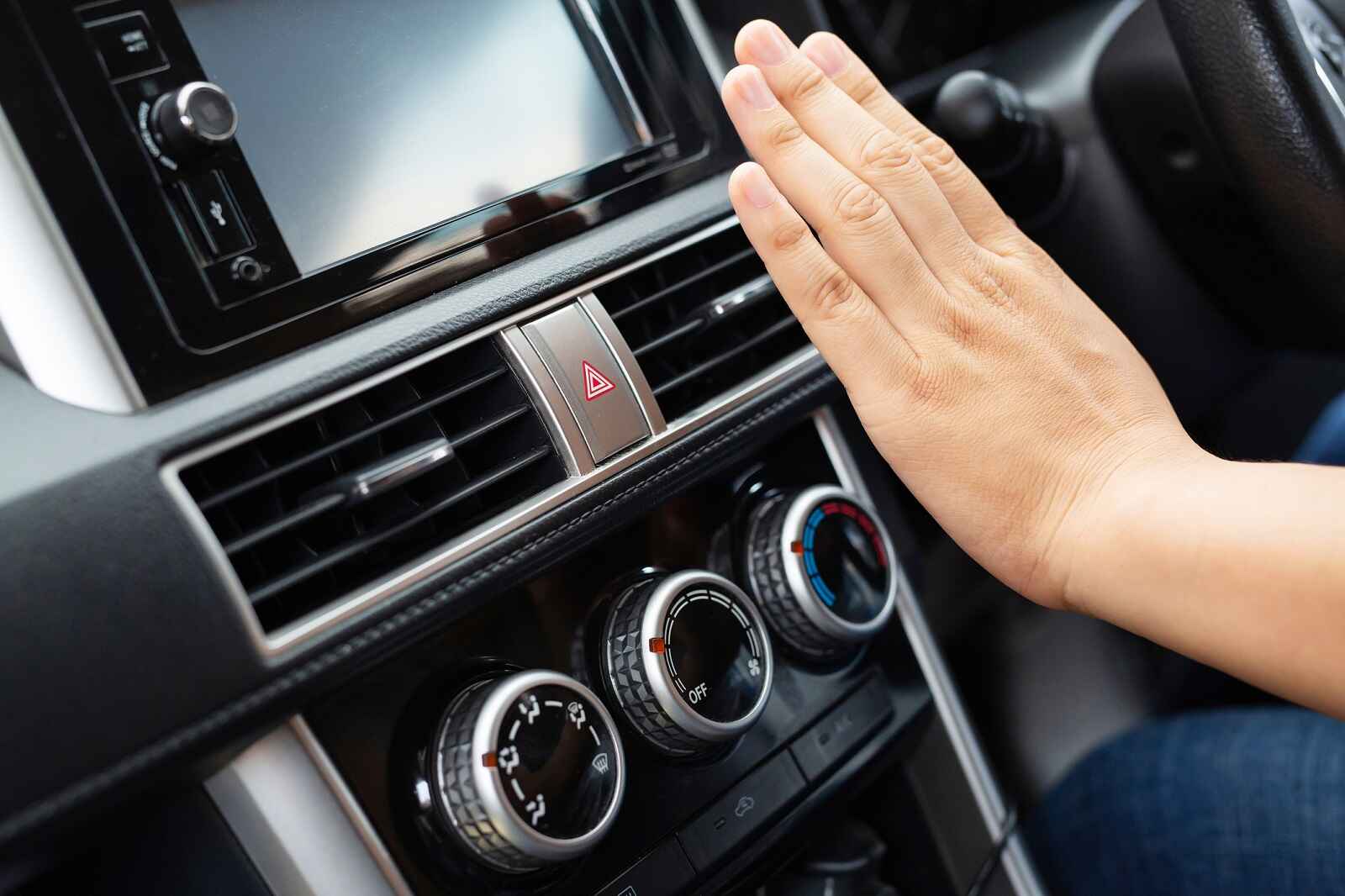 Person's hand in front of car cabin air vents feeling car AC working