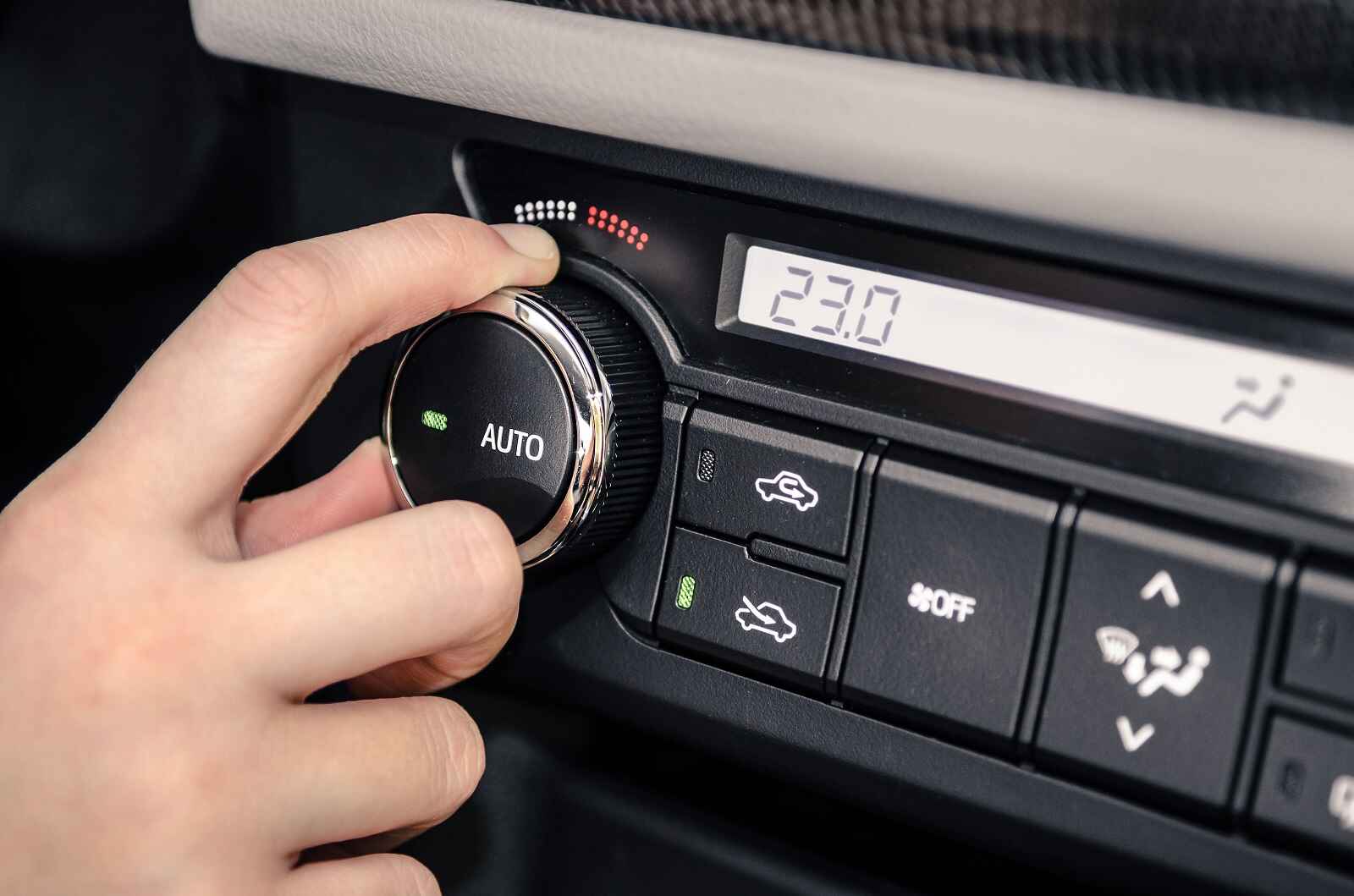 A hand adjusts a car's HVAC controls with recirculate button off