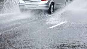 A silver car drives through heavy water on road risk of aquaplaning