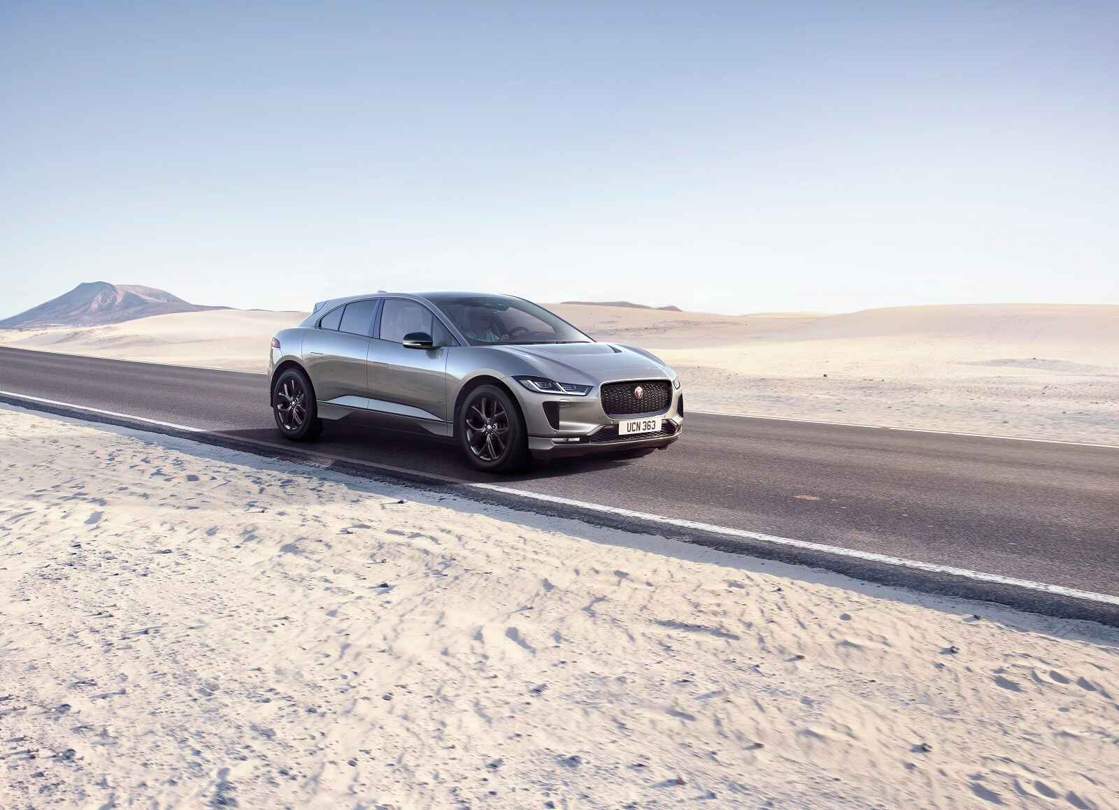 A charcoal colored Jaguar I-Pace all-electric SUV has a high market day supply in 2024 driving on a paved road in a bright desert environment