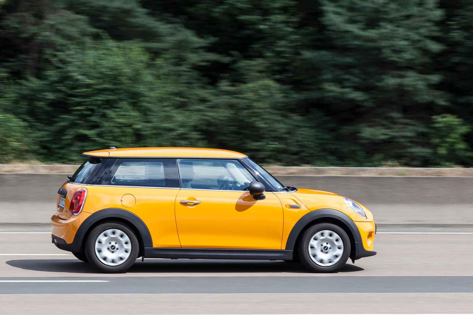 A yellow hard top MINI Cooper driving on a highway in close full right profile view