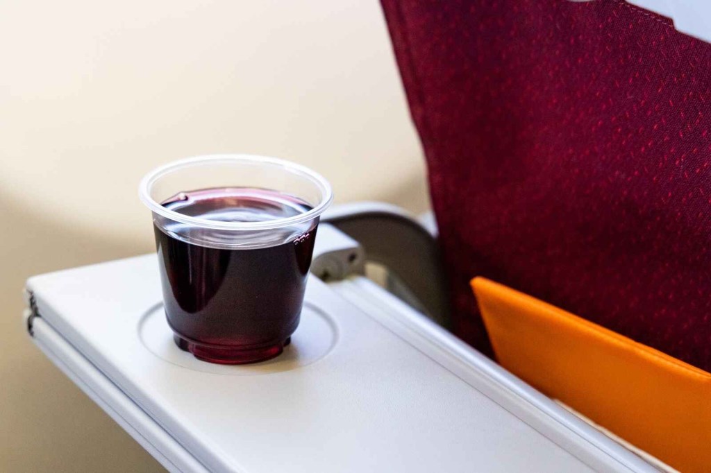 A cup a red wine sits on an airplane tray table drinking alcohol on a plane