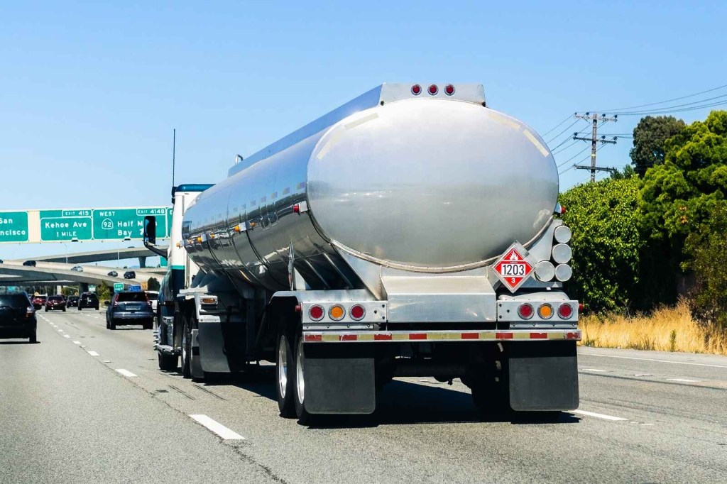 A tanker truck drives on a San Francisco highway system with green exit signs approaching