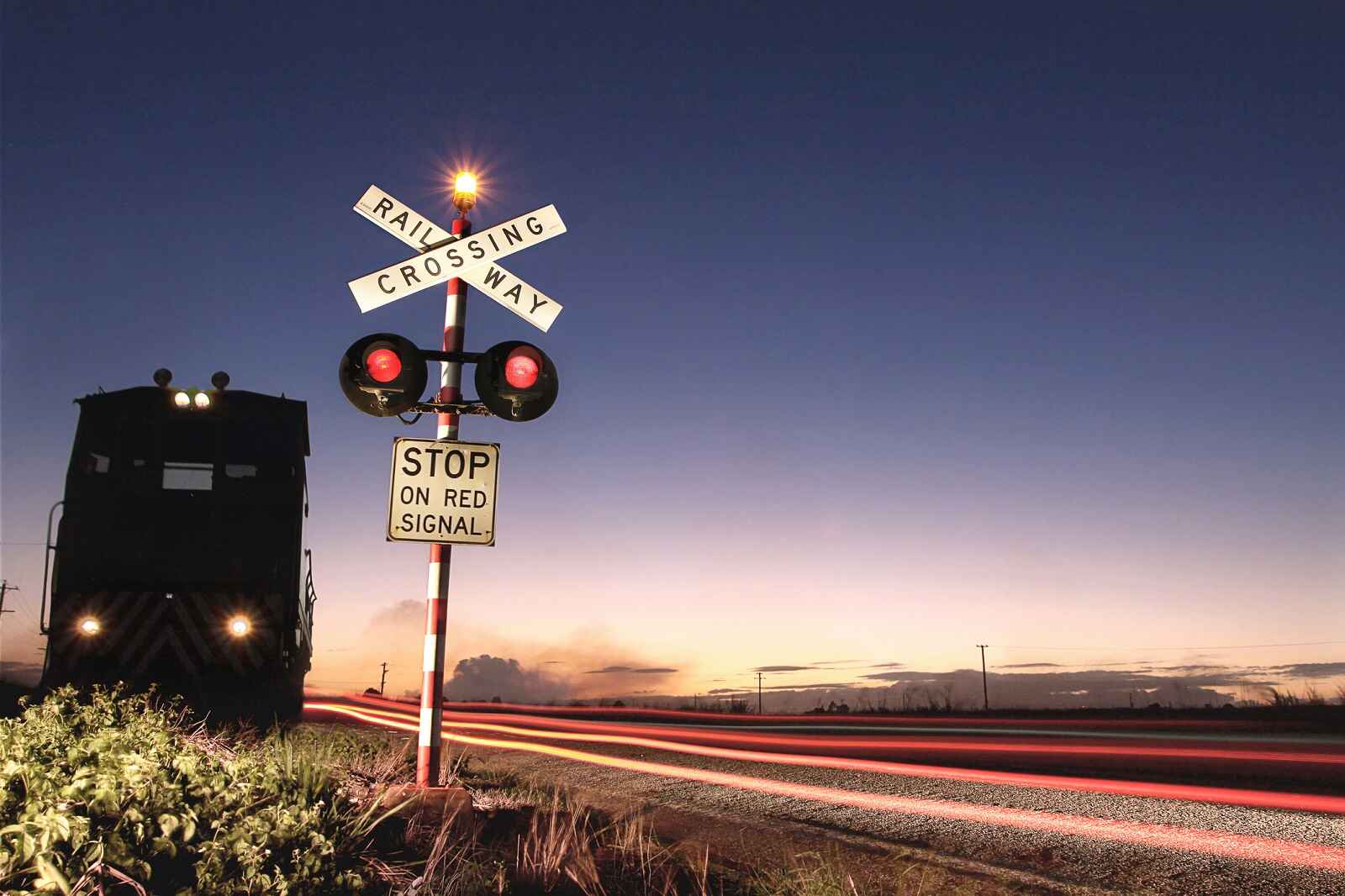 Railroad crossing sign with train moving away at dusk