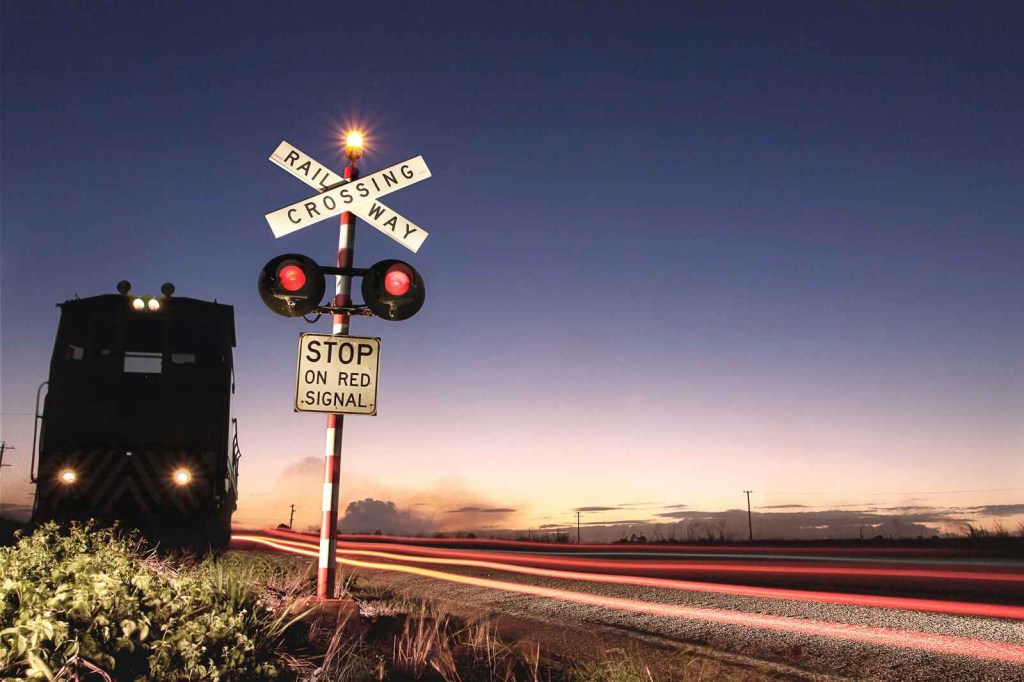 Railroad crossing sign with train moving away at dusk