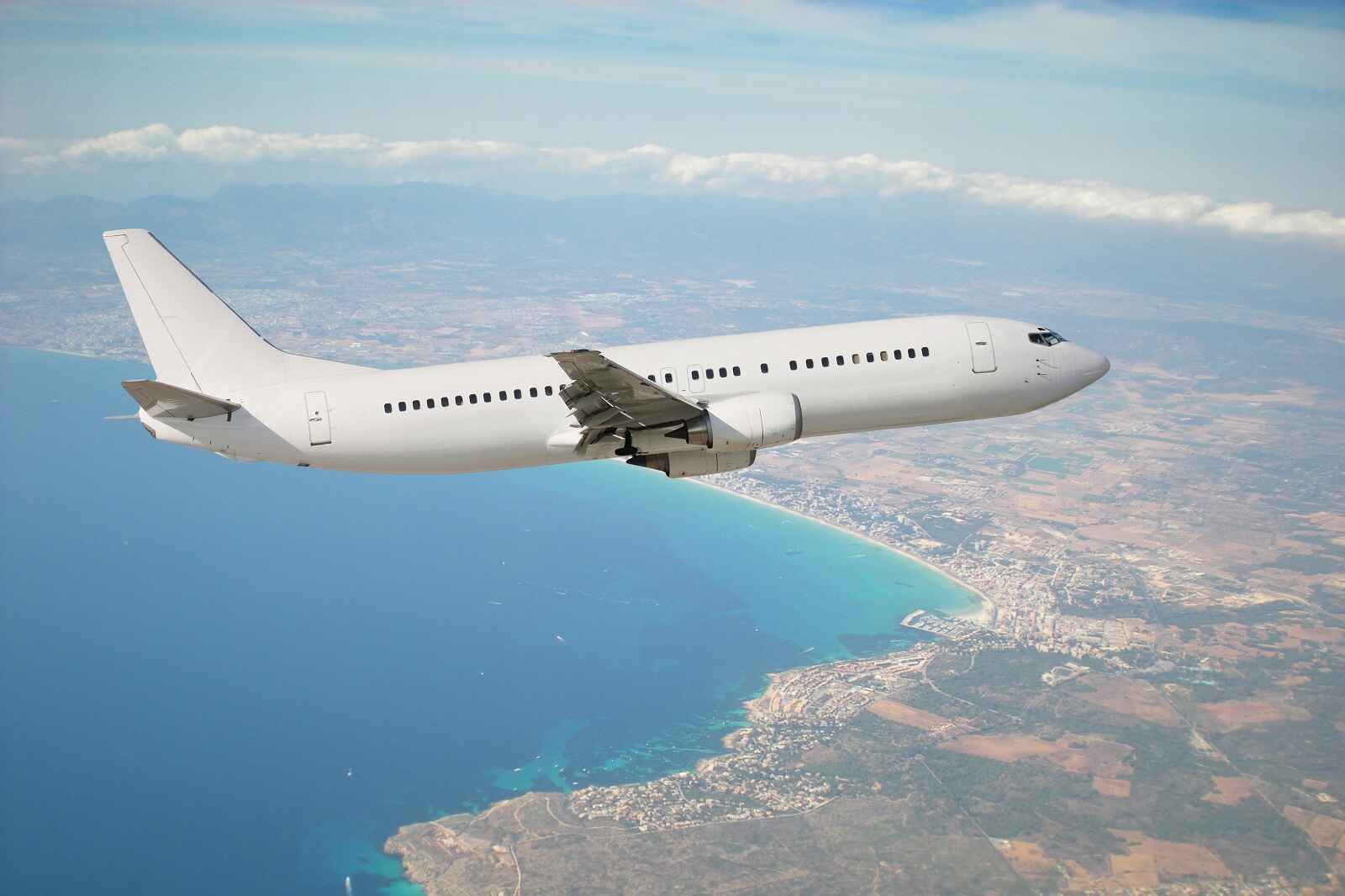 White passenger airplane flying from above ocean into coastal region