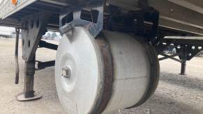 Silver round tank hung beneath a semi truck trailer.