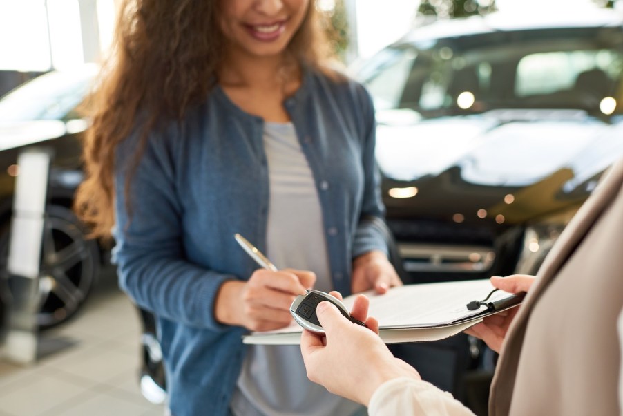 Woman signs a rental car contract as she's handed the keys, in a parking lot.