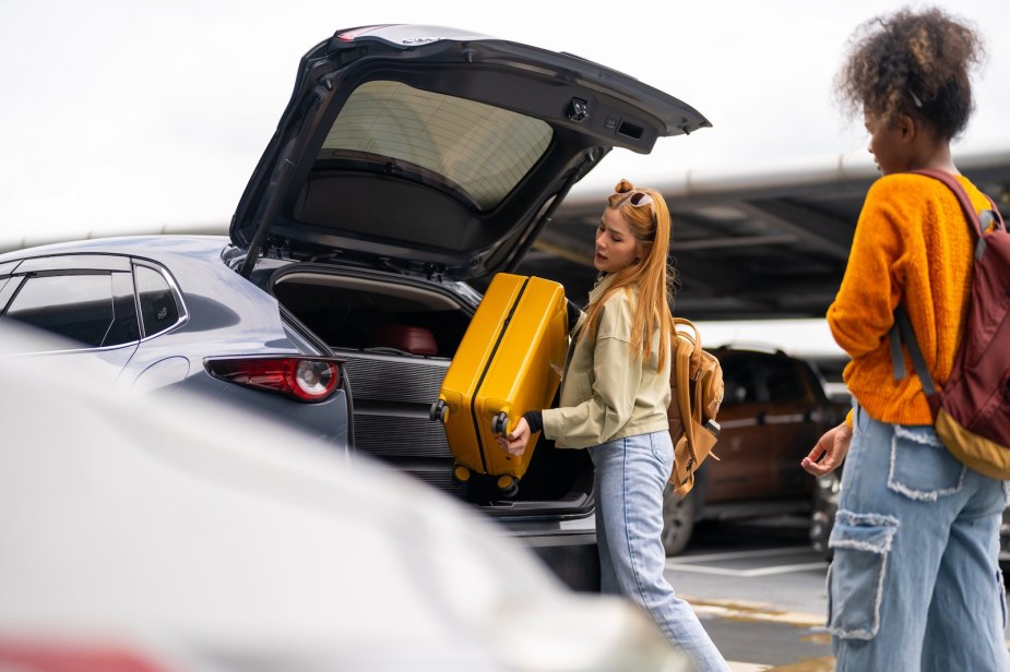 Two women load luggage into a hatchback rental car.