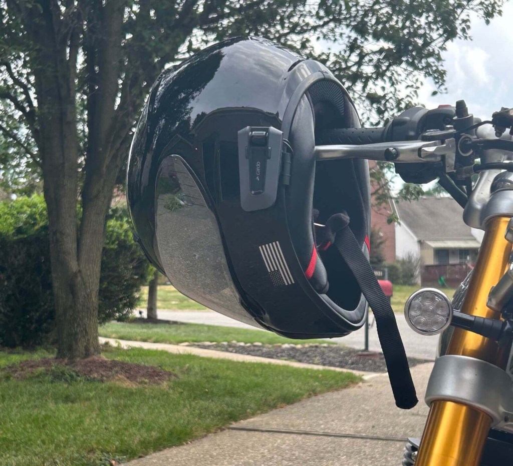 A SHOEI RF-SR motorcycle helmet with a Cardo PACKTALK EDGE Bluetooth unit on a set of handlebars.